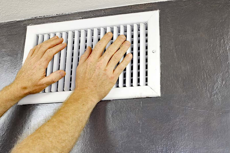 Hands feeling hot air blow out of white vent