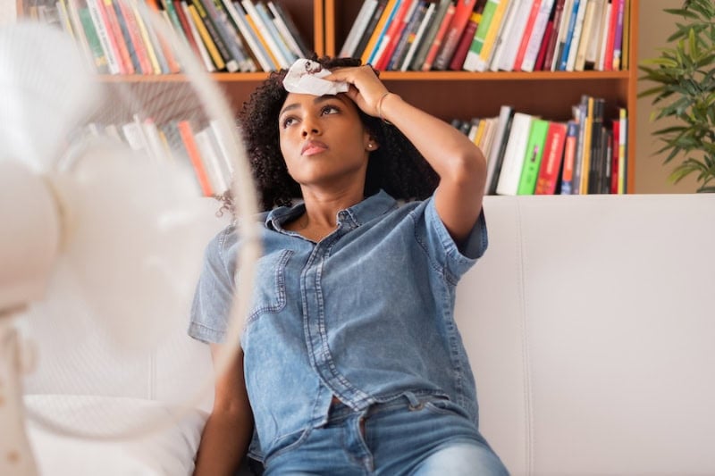 Common AC Problems and Solutions. Black woman sweating and trying to refresh at home.