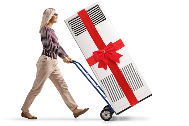 When Do I Replace My Air Conditioner? - Full length profile shot of a woman pushing a hand-truck with a self standing ac unit tied with red ribbon isolated on white background