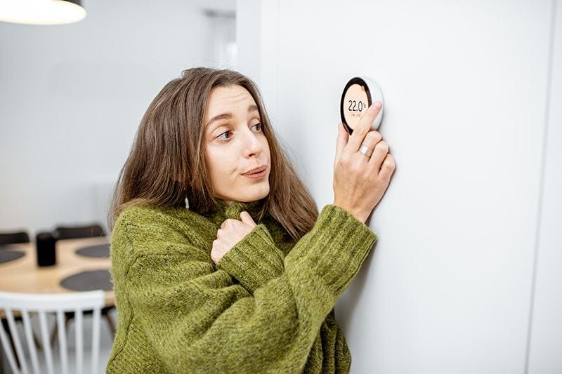 Female homeowner feeling cold and adjusting thermostat, because her heat pump keeps turning off.